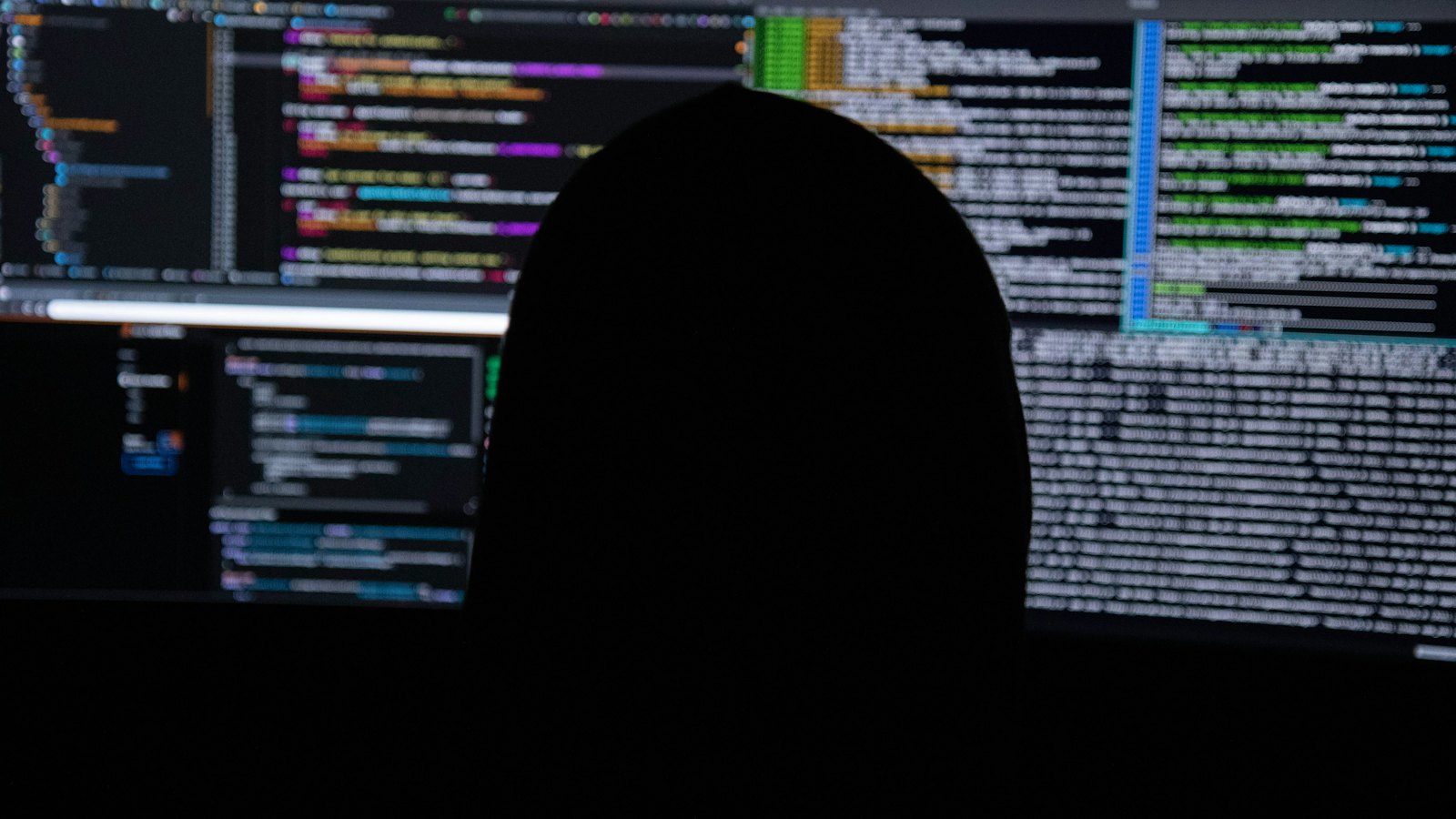 A person in silhouette in front of computer screens full of code