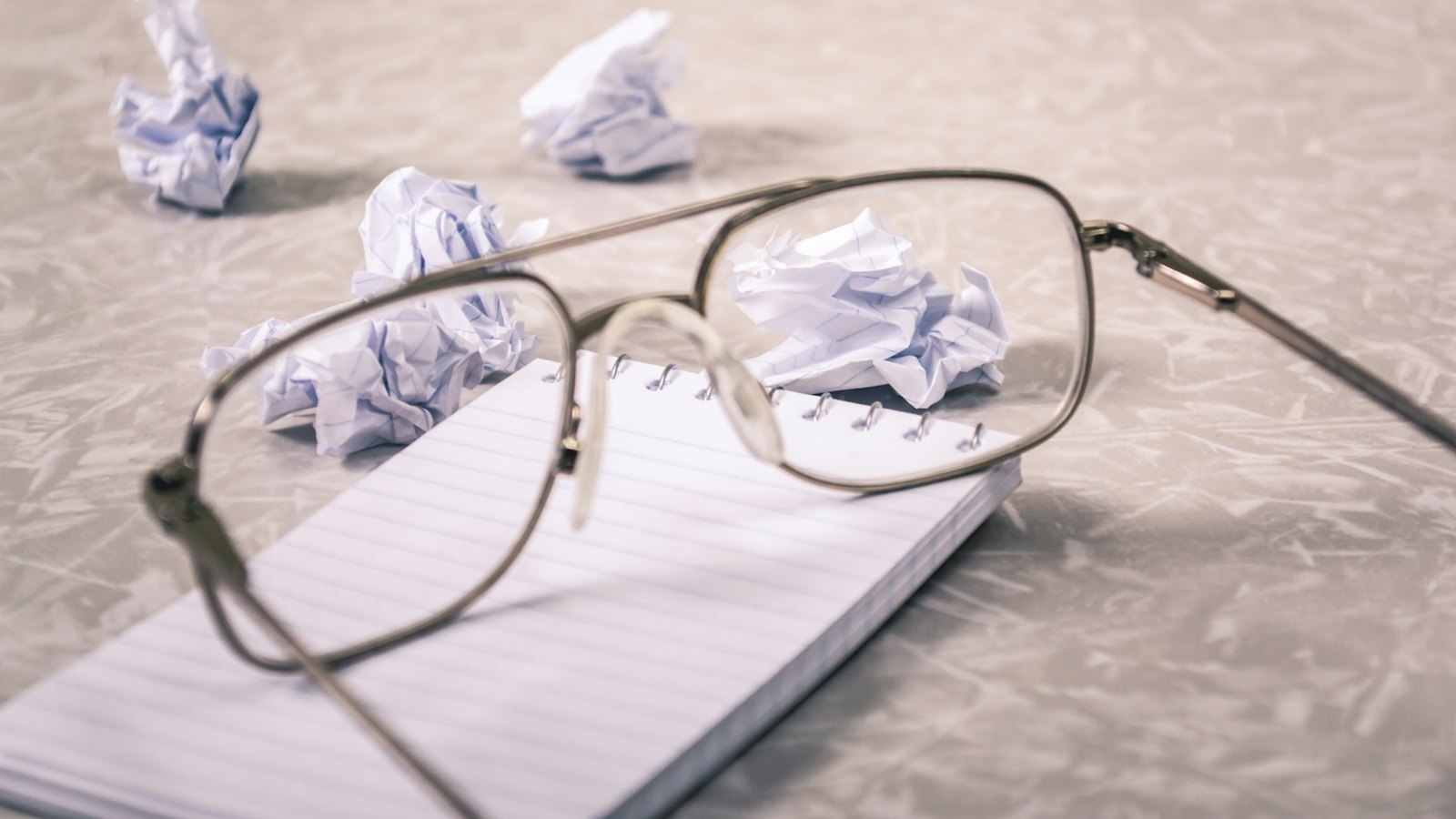 Glasses on a notepad beside crumpled paper