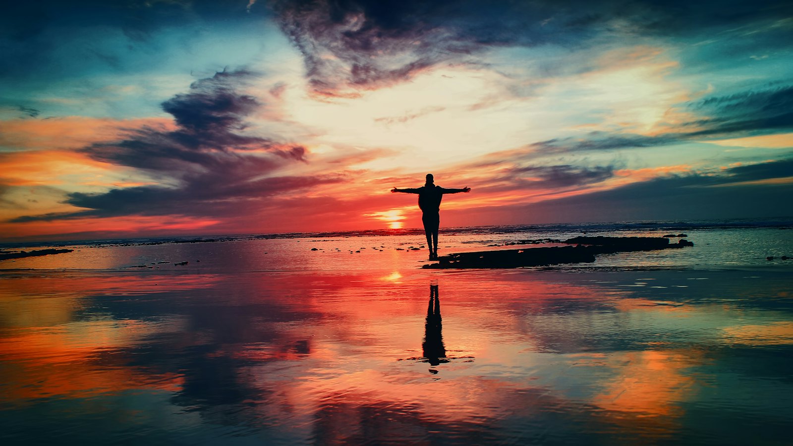 A person with arms outstretched by the water at sunset
