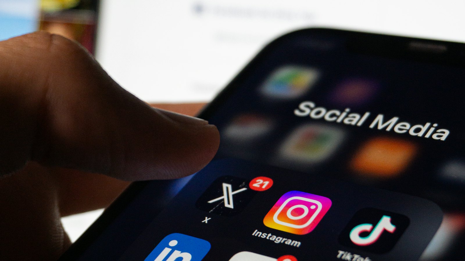 A hand holding a phone with a social media folder including X and TikTok