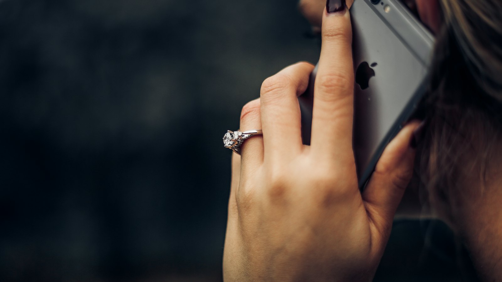Close-up of a hand holding a phone to an ear against a dark background