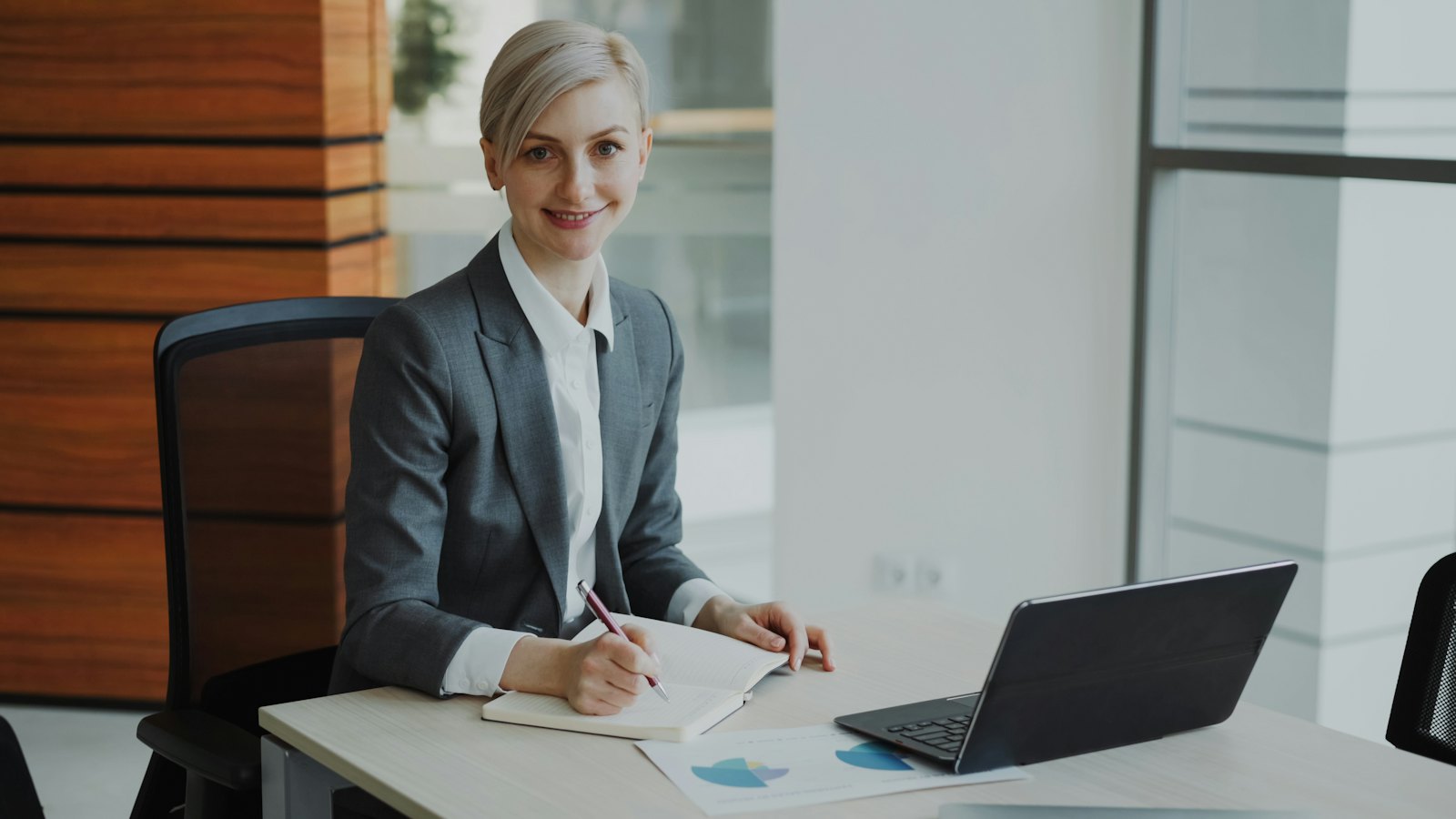 A smiling professional at a desk with a laptop