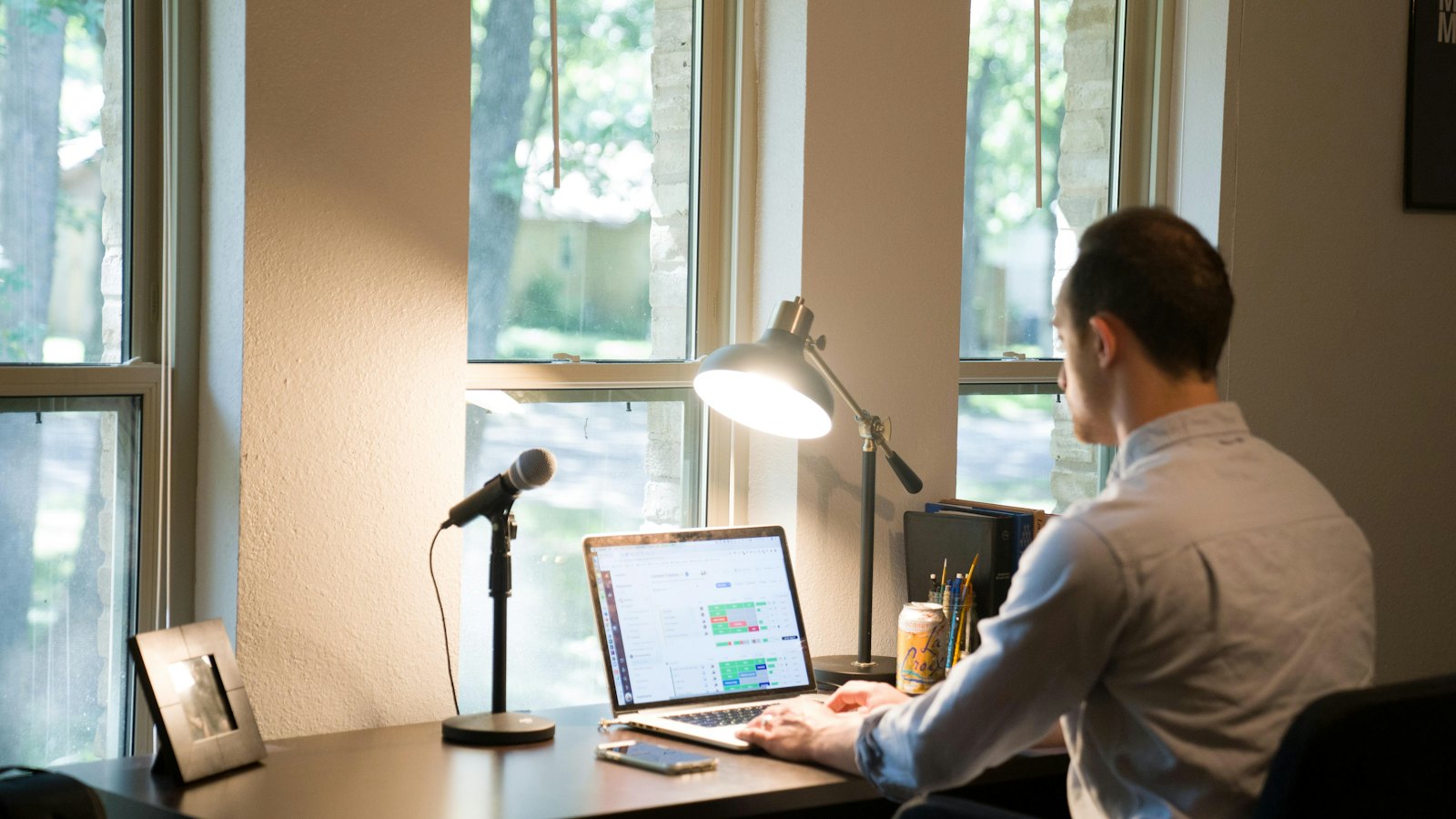 A man working at a laptop on a desk by a sunny window