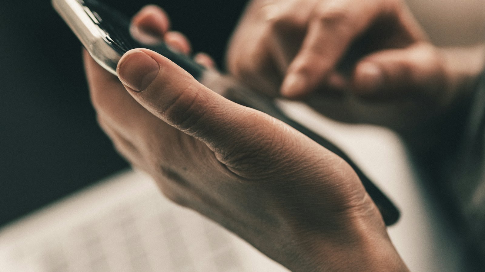 Hands holding a smartphone above a laptop keyboard
