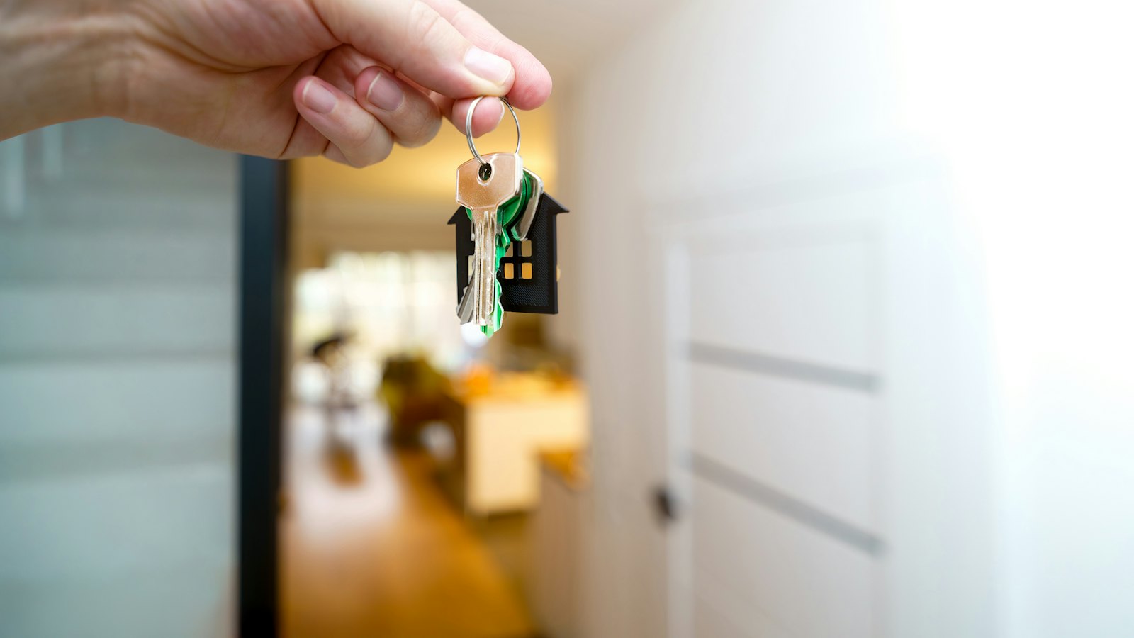 A hand holding house keys with a small house-shaped keyring