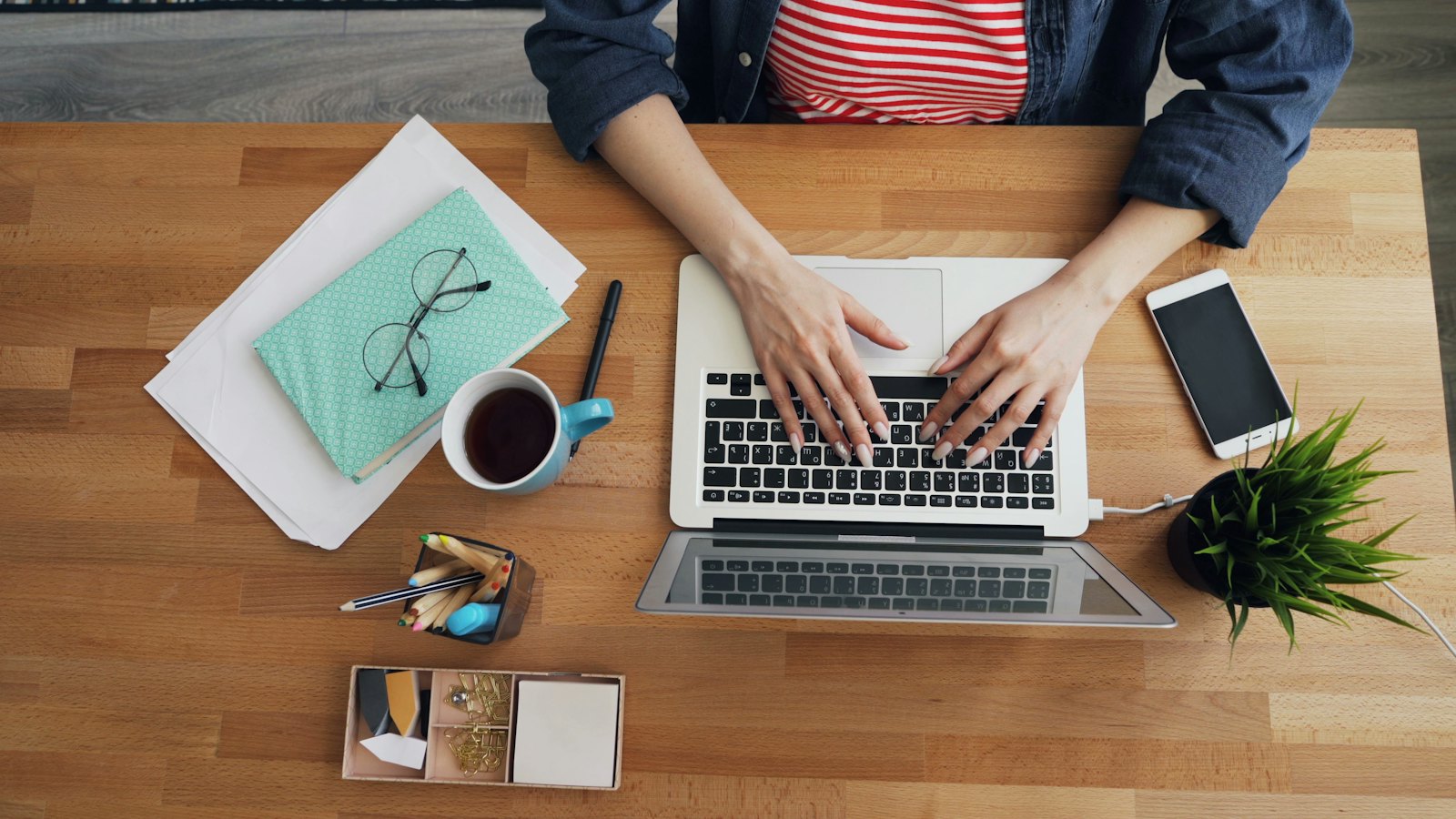An overhead view of a person typing on a laptop at a wooden desk