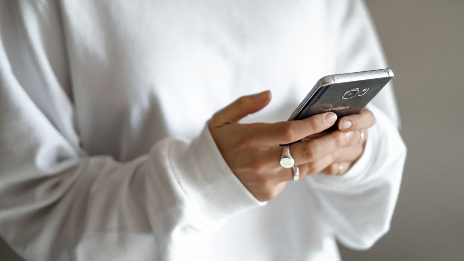 A person in a white jumper typing on a smartphone