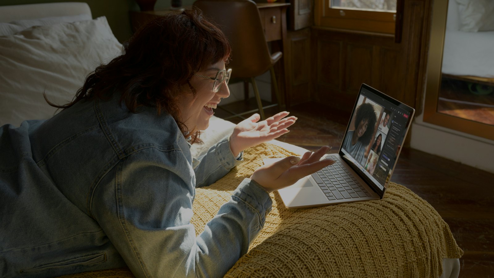 A woman lying on a bed talking to someone on a video call on her laptop