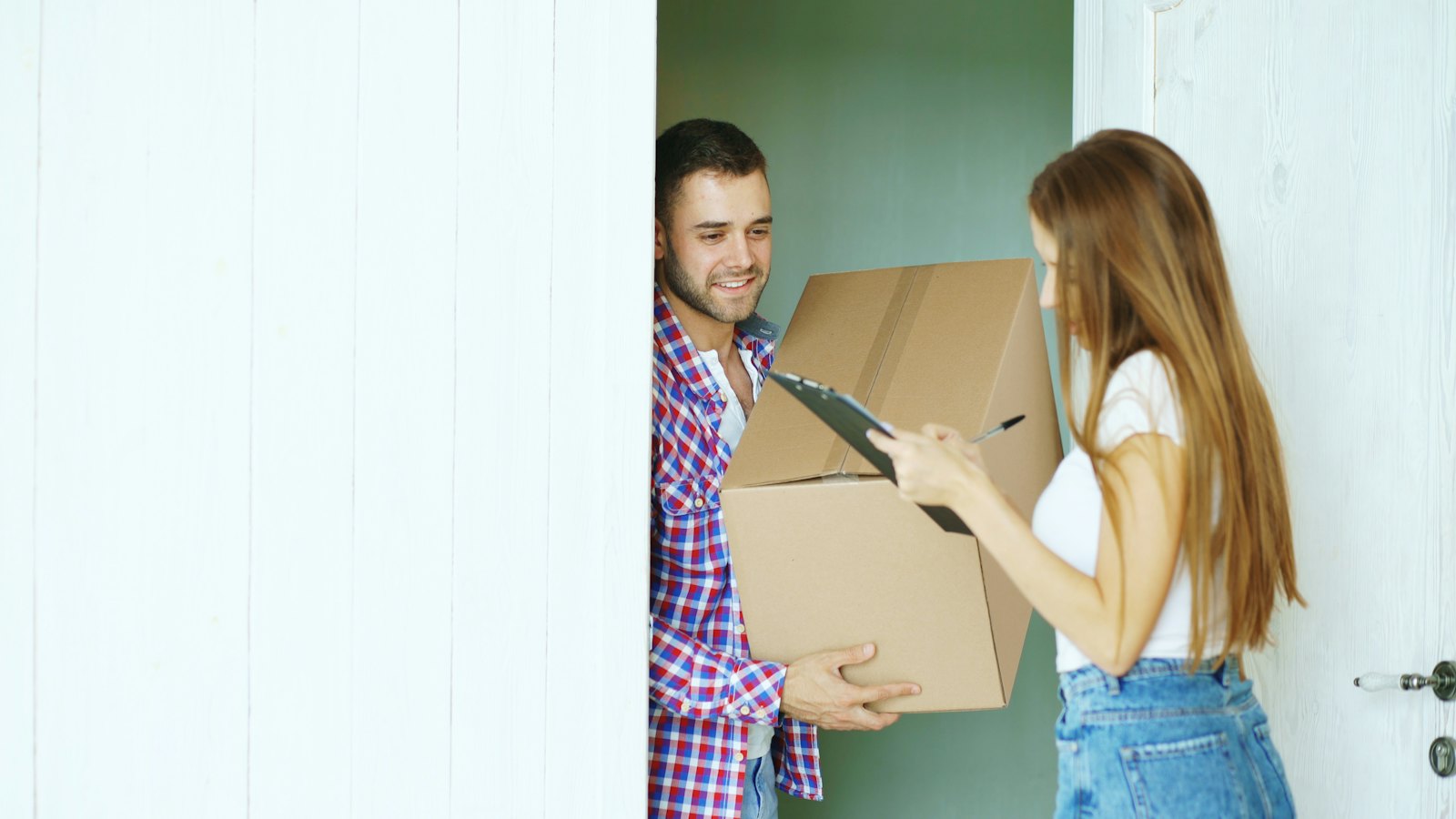 A woman at her front door signing for a parcel held by a delivery man