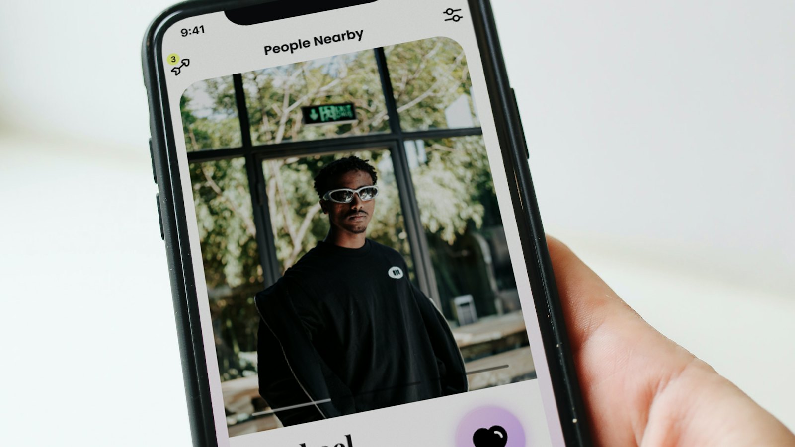 A hand holding a phone showing a dating app profile of a man