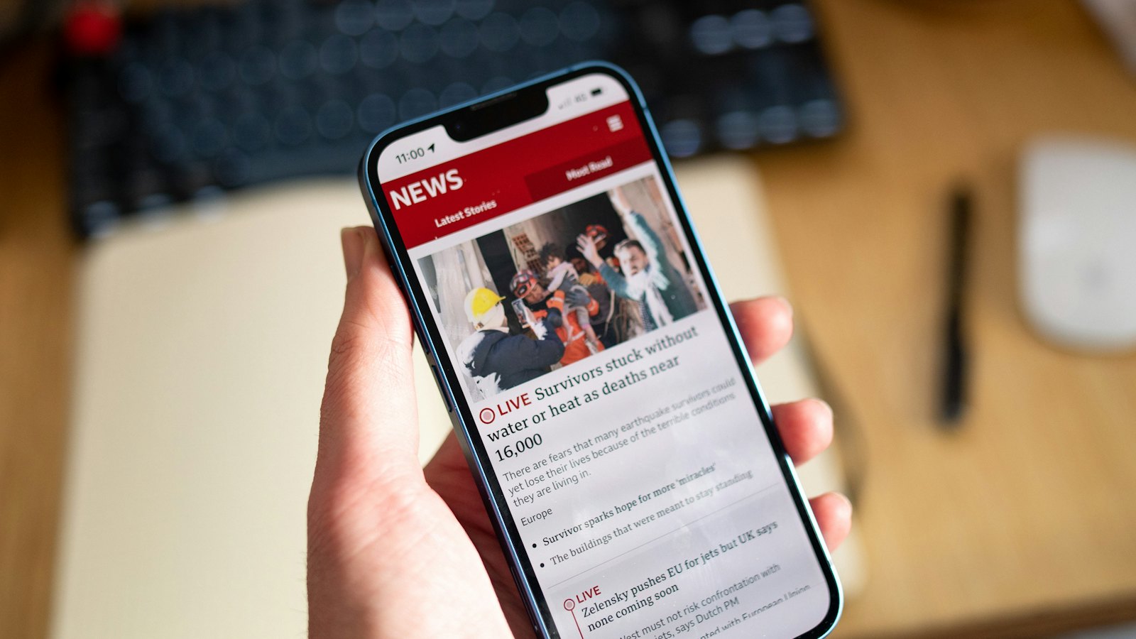 A hand holding a phone showing a news feed with images