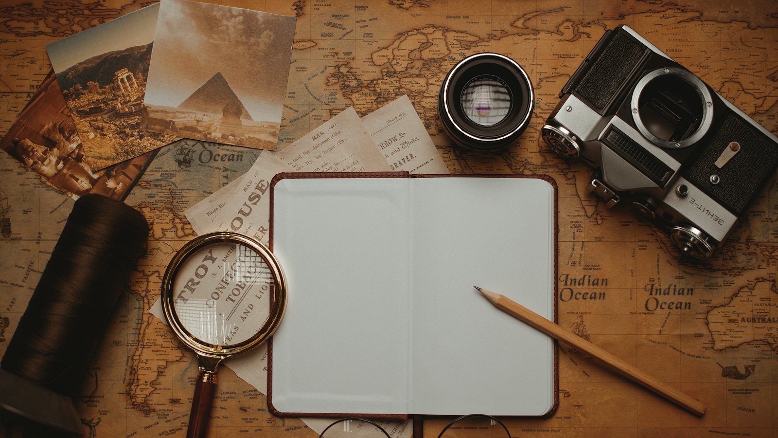 A magnifying glass, an open notebook and a camera laid out on an old map