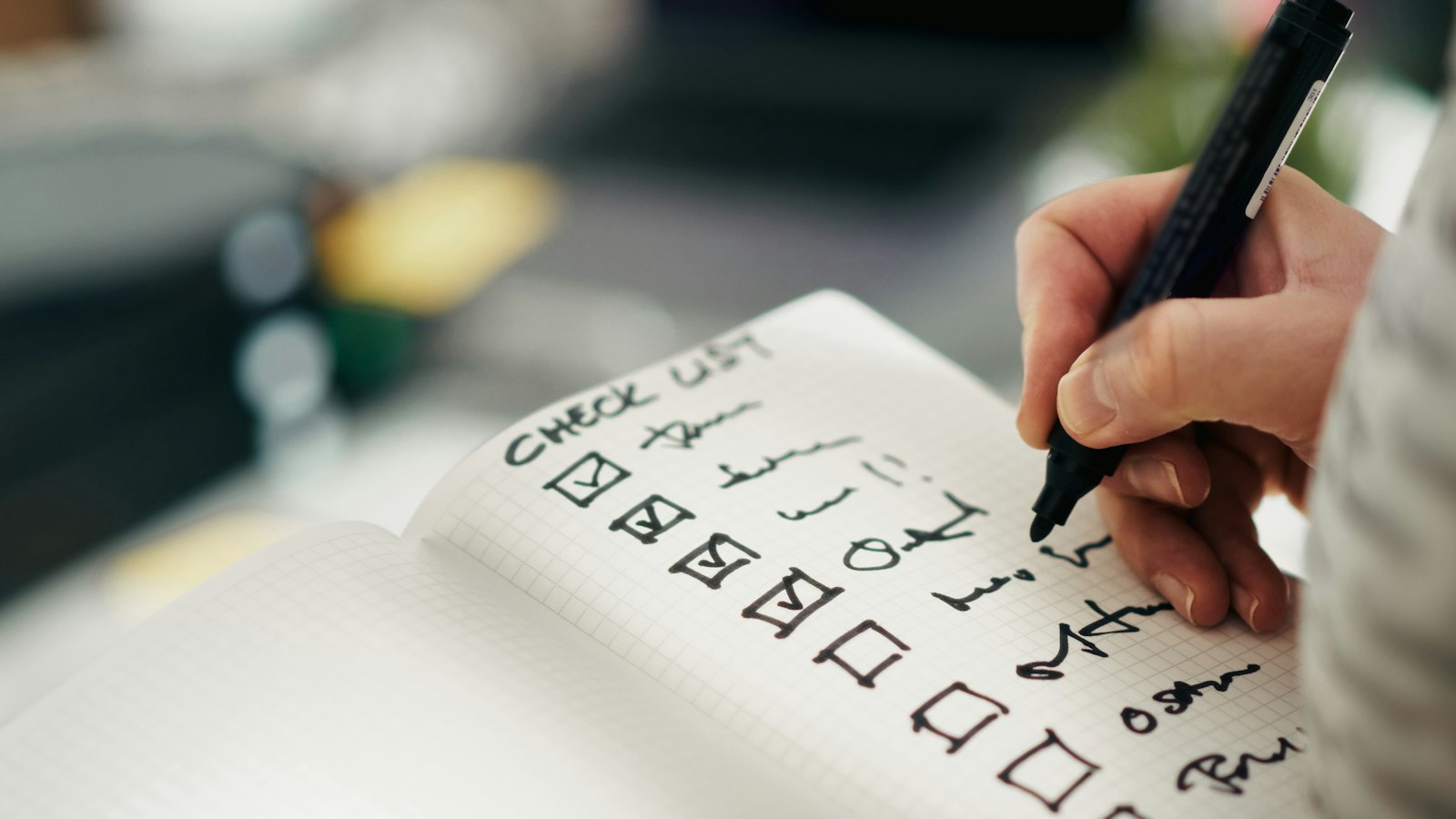 A hand ticking boxes on a handwritten checklist in a notebook