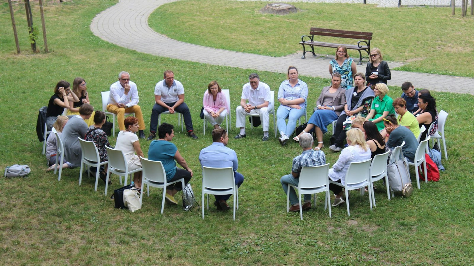 A community group sitting in a circle of chairs on a lawn
