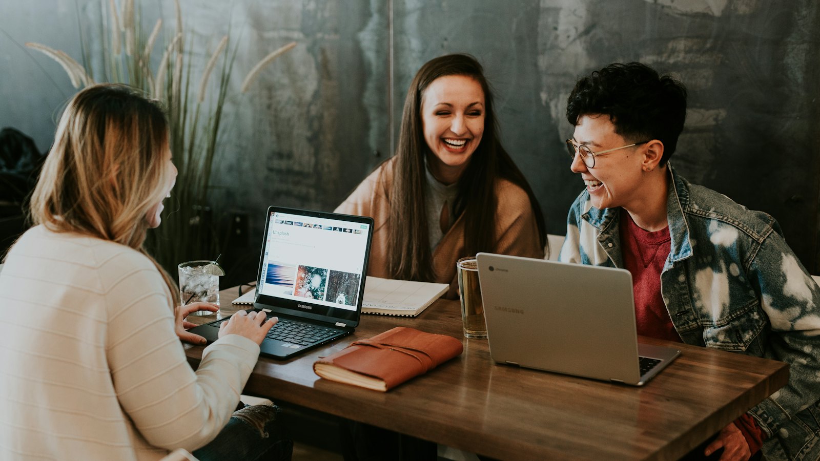 Three students laughing together at a table with laptops