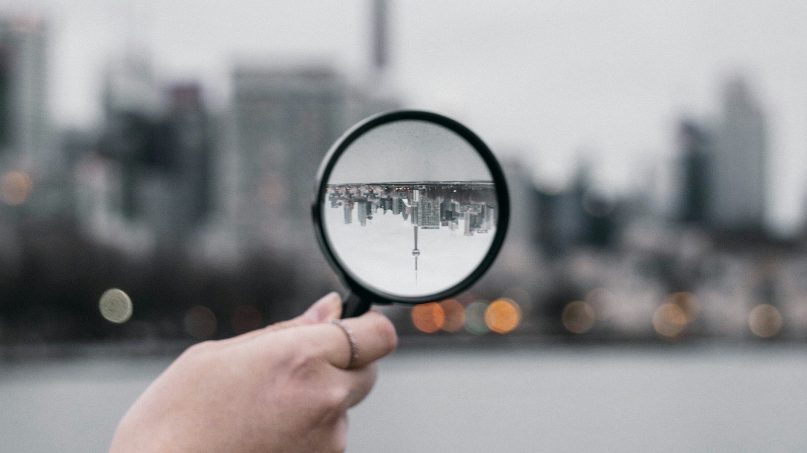 A hand holding a magnifying glass against a city skyline