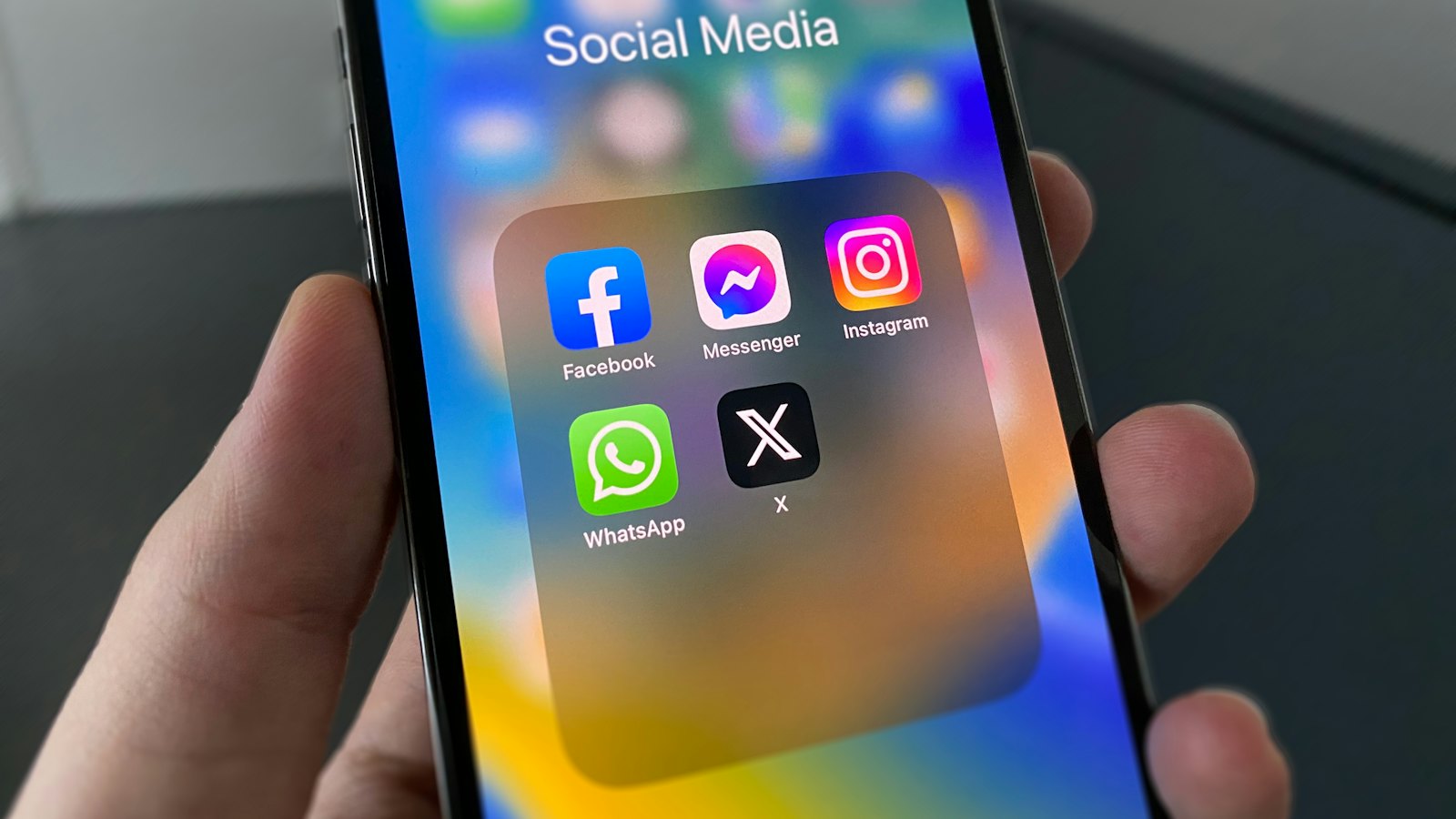A hand holding a phone showing a folder of social media apps