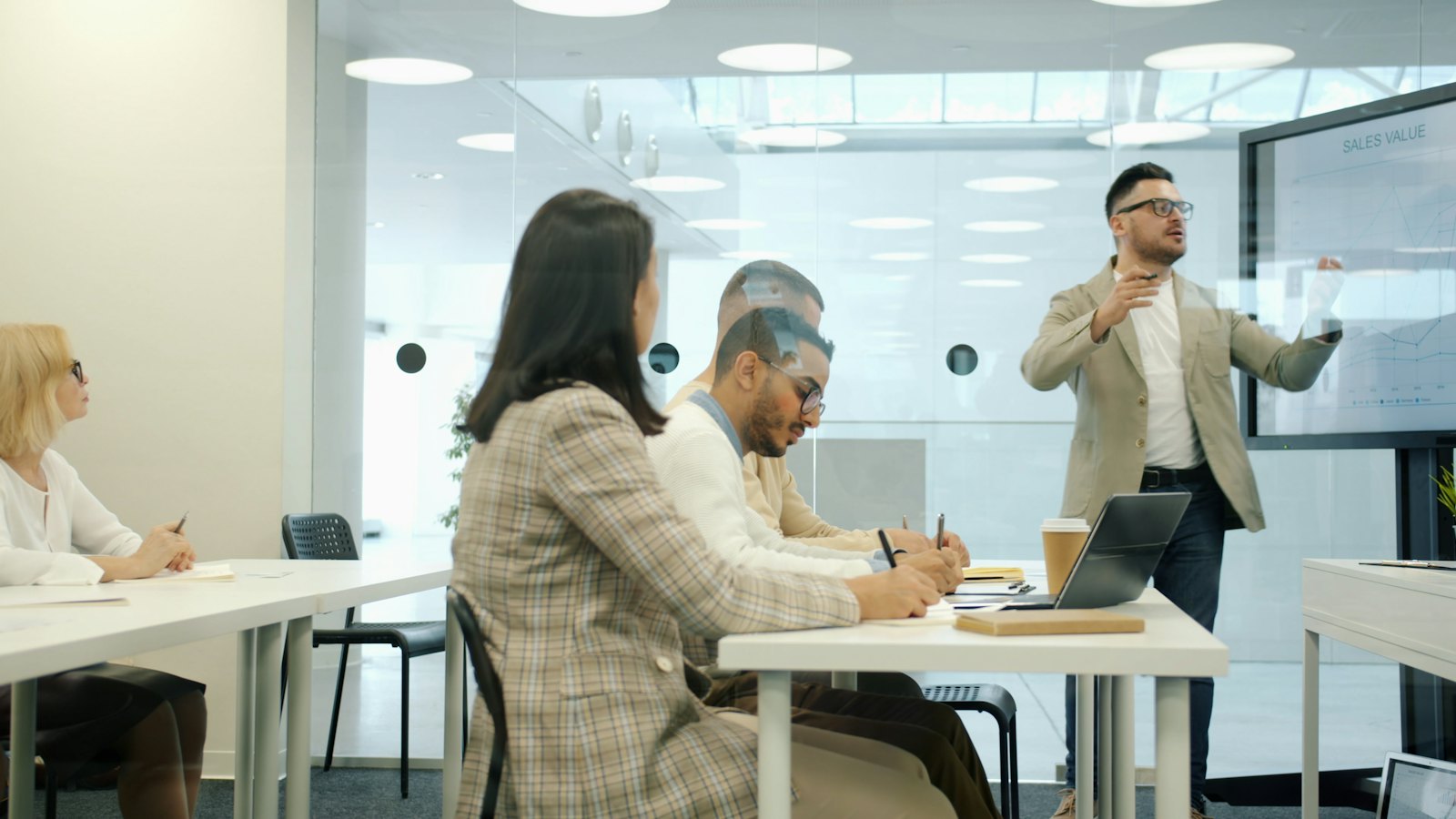 A presenter speaking to colleagues seated at desks in a bright office training room
