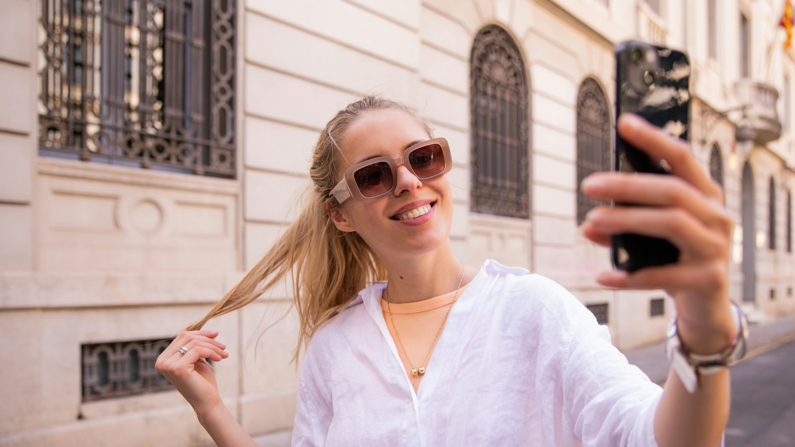 A smiling woman taking a selfie on a city street