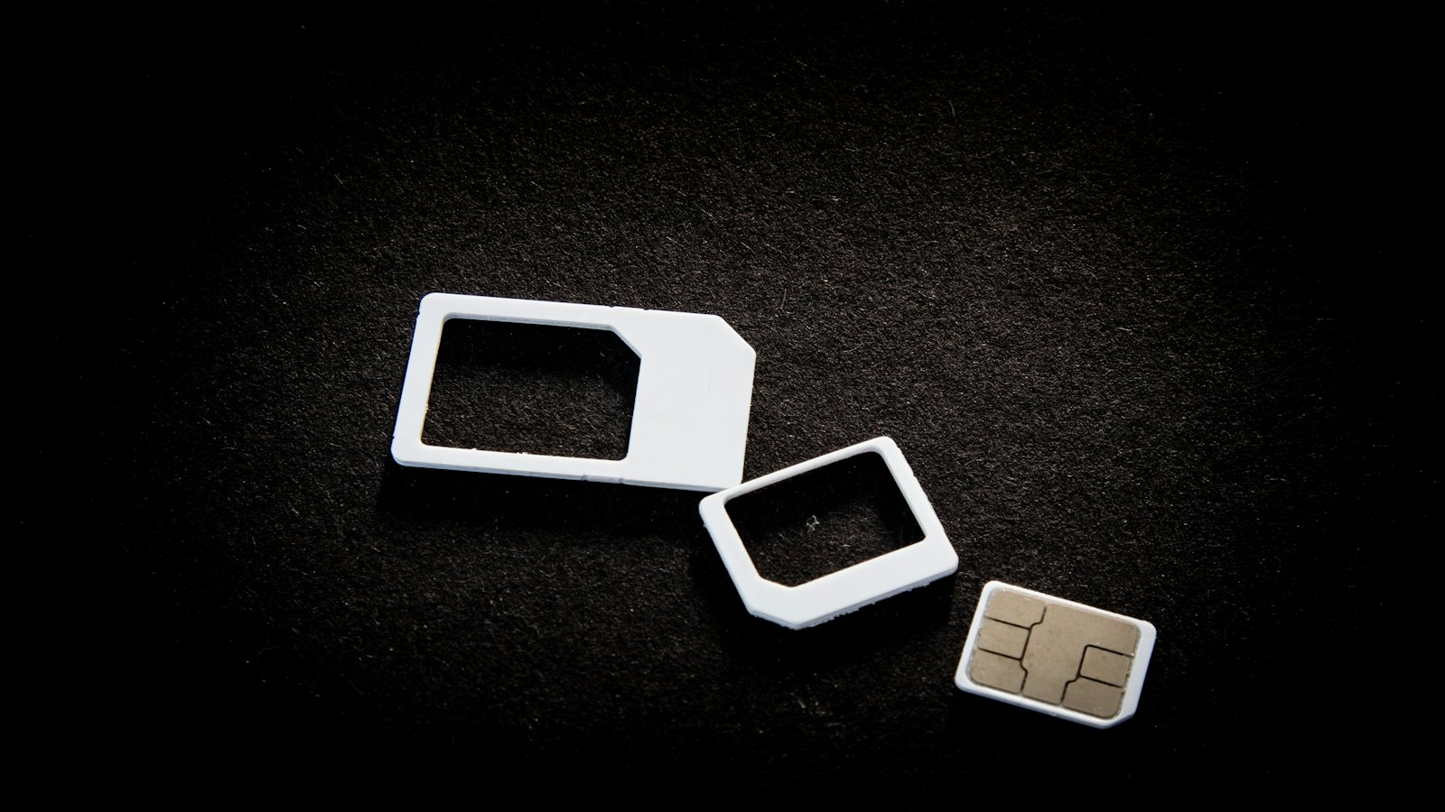 A SIM card and its adaptor frames on a black surface