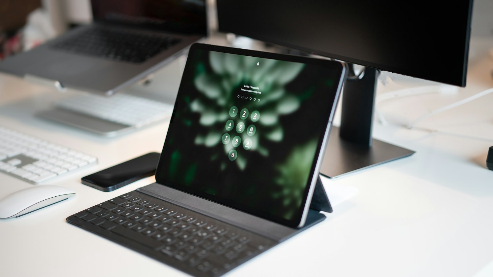 A tablet with a keyboard case on a bright desk beside a monitor