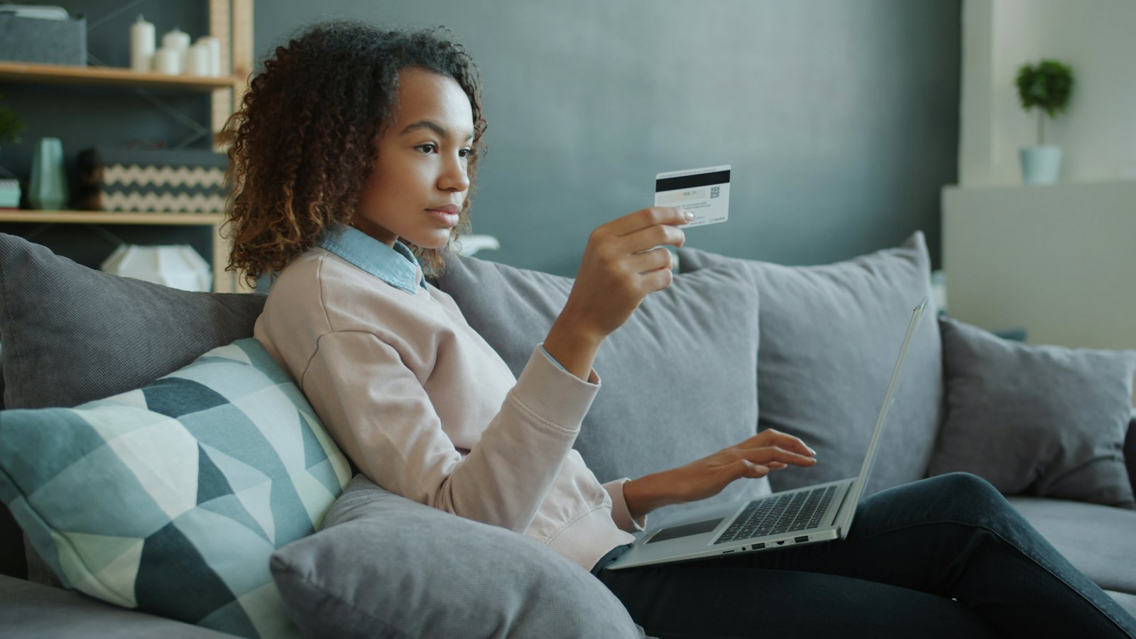A woman on a sofa shopping online with a laptop and a card