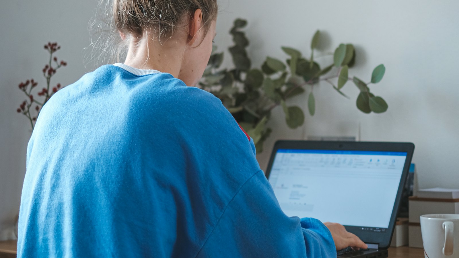 A woman in a blue jumper working at a laptop