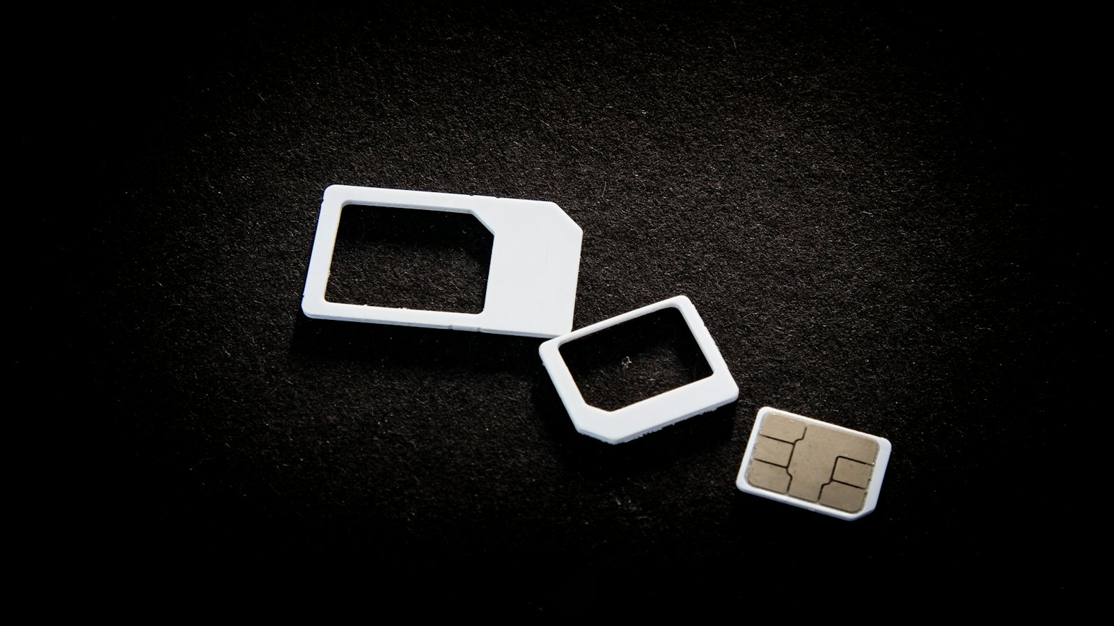 Three SIM cards of different sizes on a dark surface