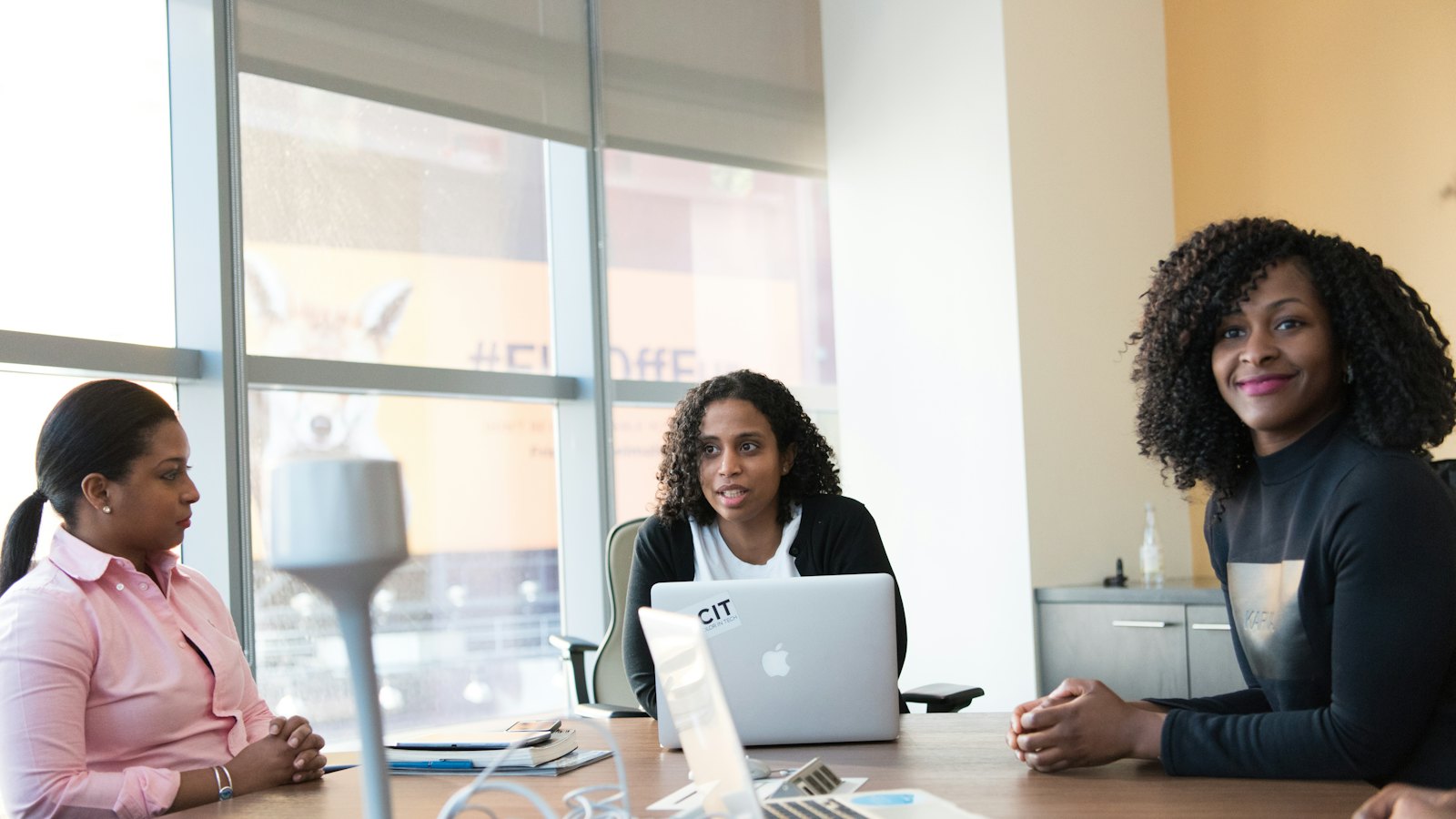 Three colleagues around a meeting table with laptops, one of them speaking