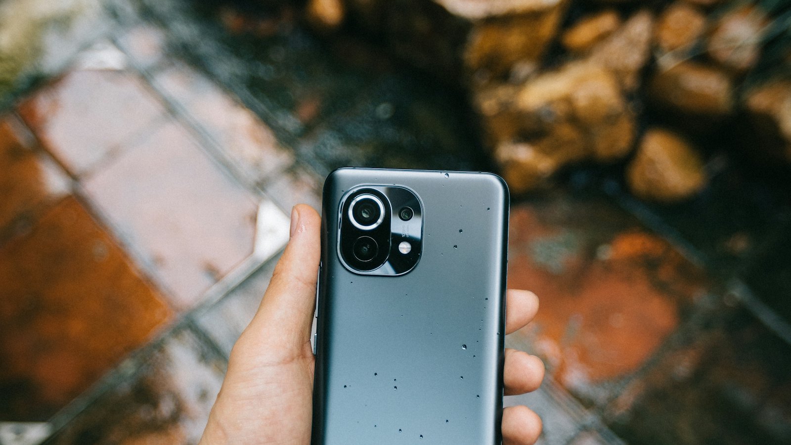 A hand holding a phone above wet paving stones