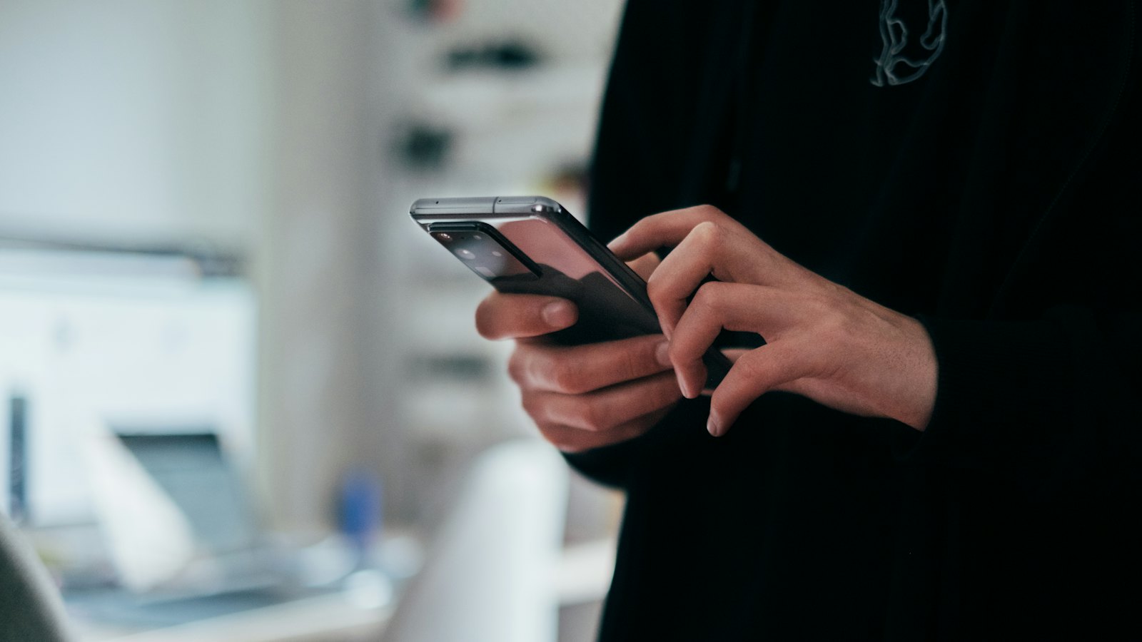 A person in a dark jumper holding a smartphone in both hands