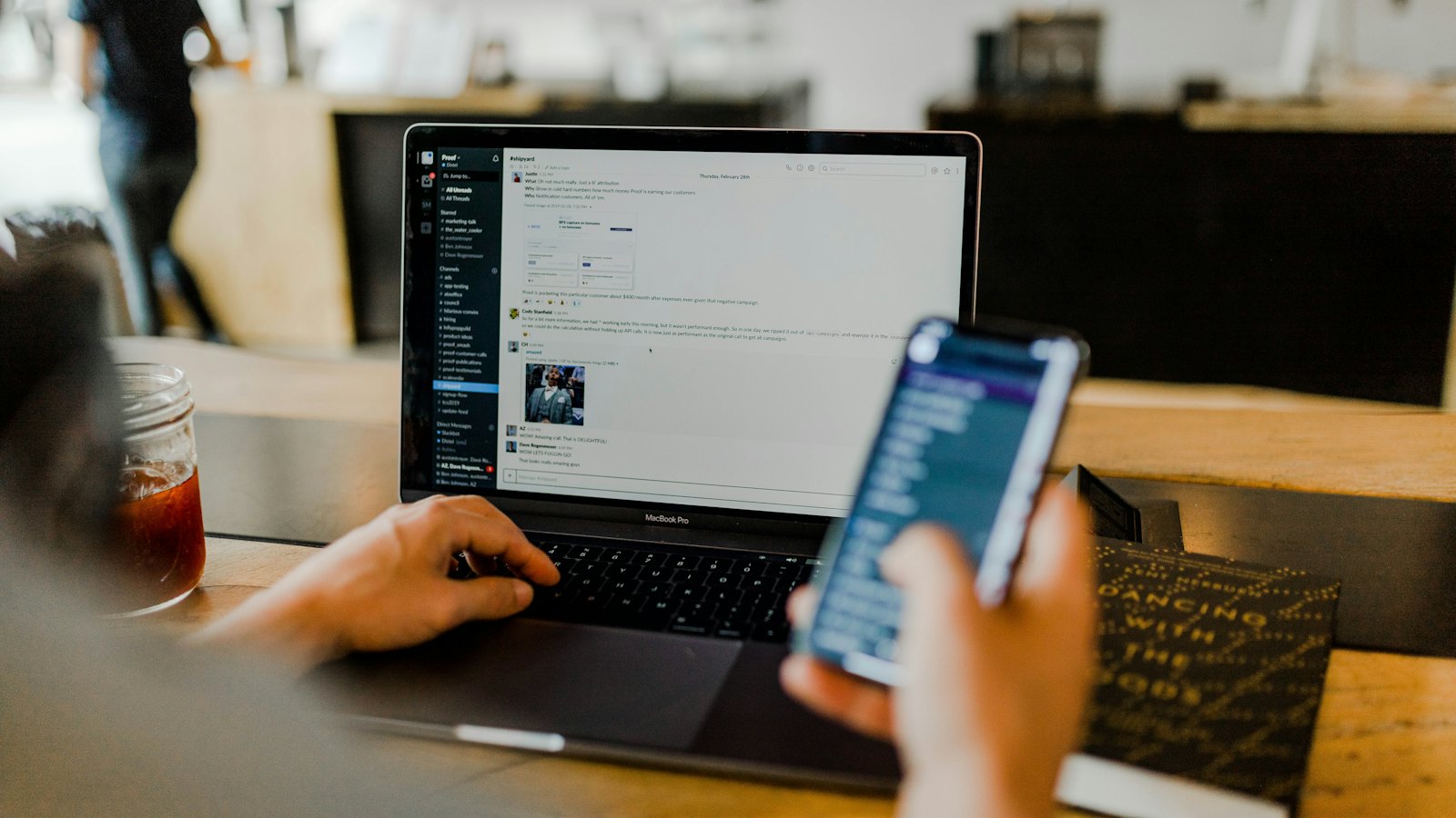A person scrolling on a phone while working at a laptop