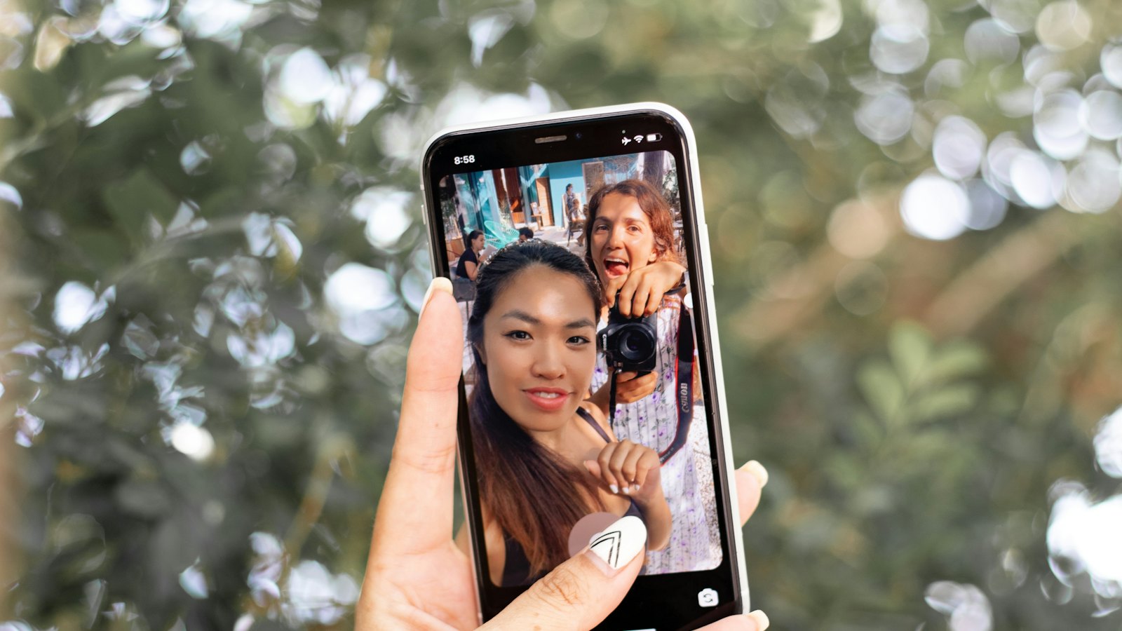 A hand holding up a phone showing a selfie of two friends
