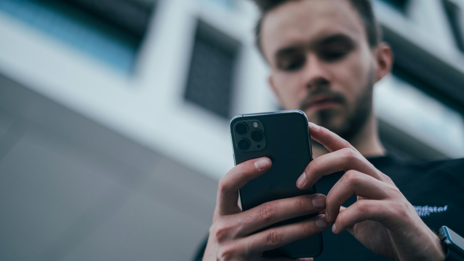 A man looking down at his smartphone in front of a modern building
