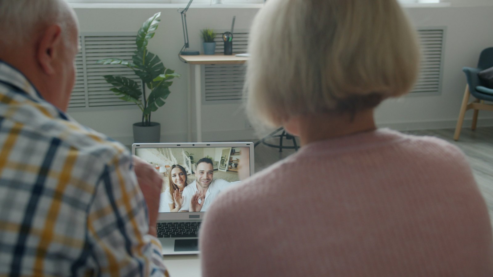 An older couple watching a video call with younger relatives on a laptop