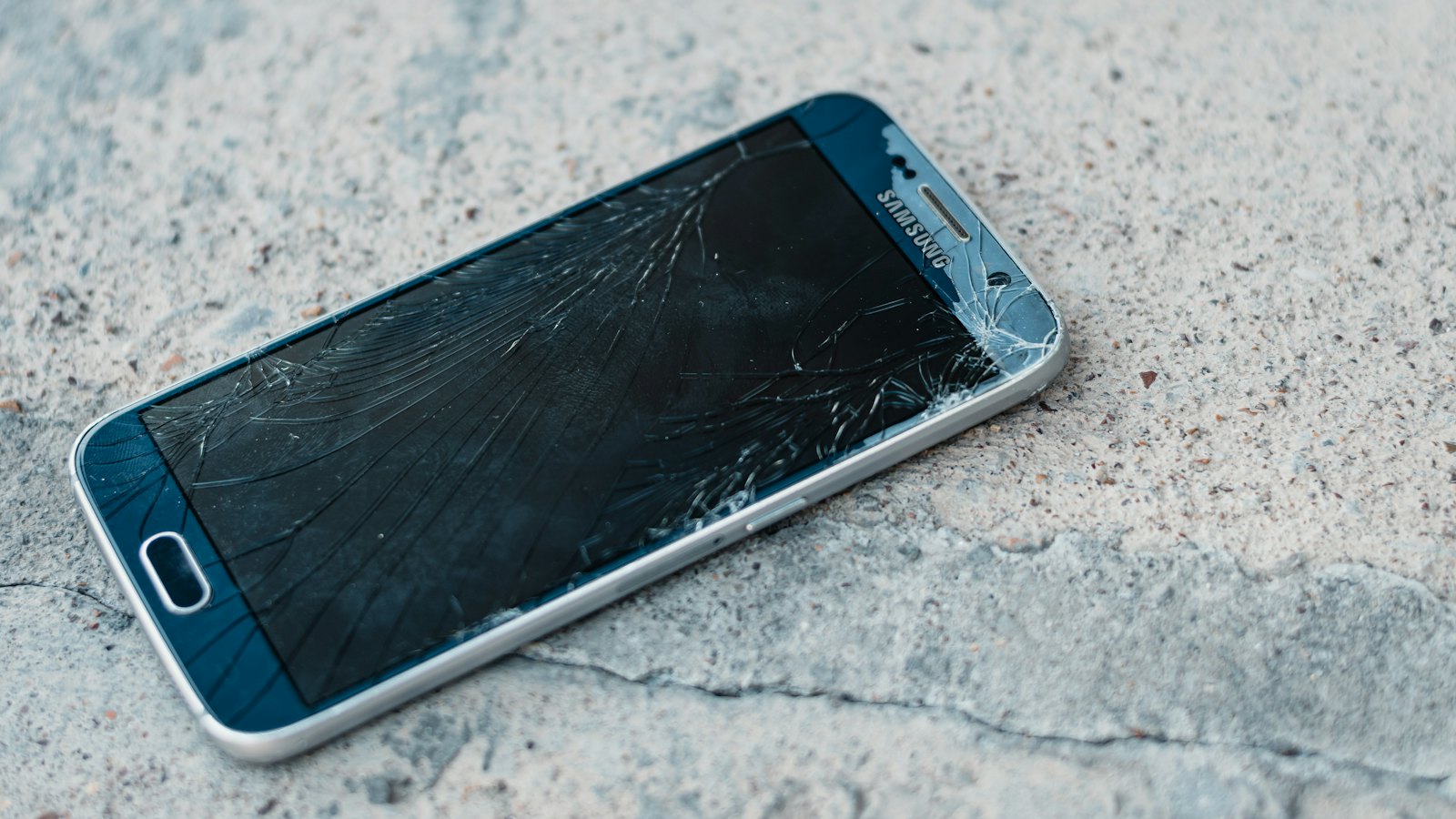 A phone with a cracked screen lying on a pavement