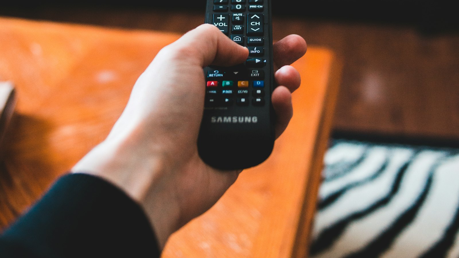A hand holding a remote control in front of a television