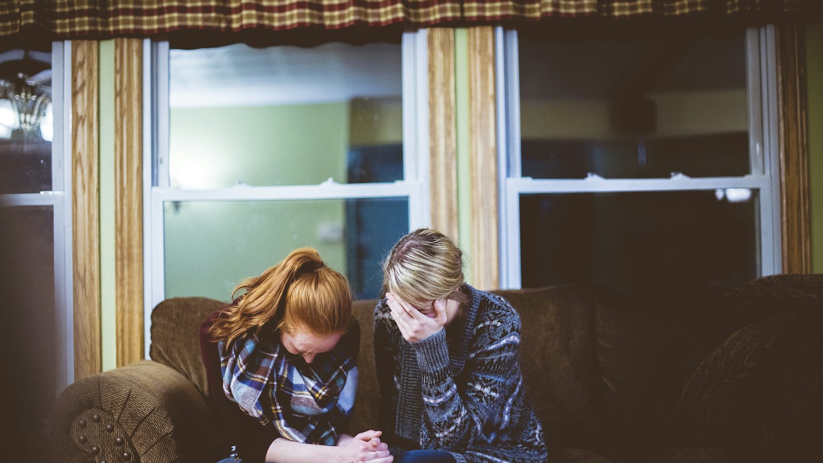 Two people sitting close together on a sofa, one comforting the other