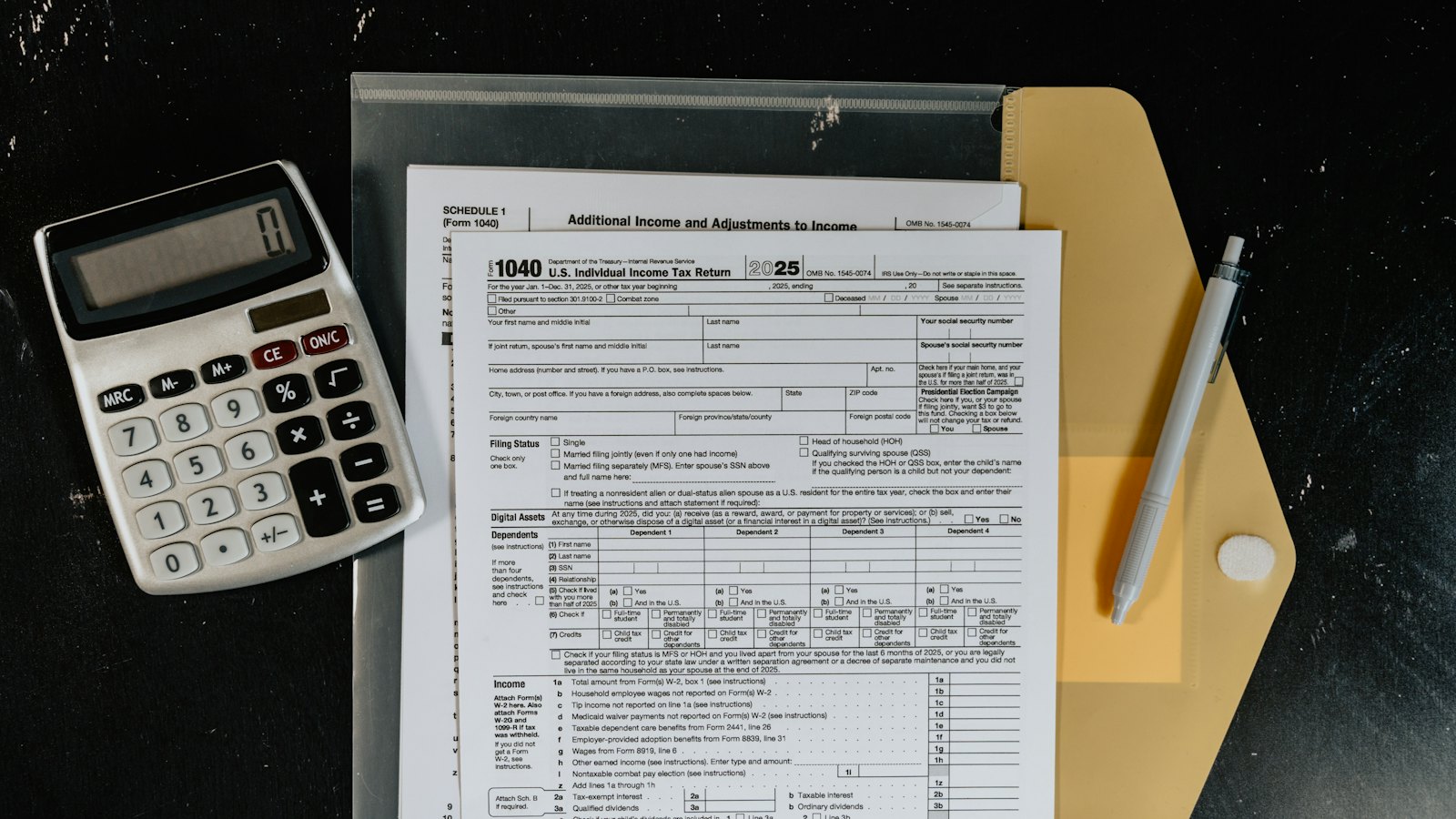 Tax forms, a calculator and a pen on a dark surface