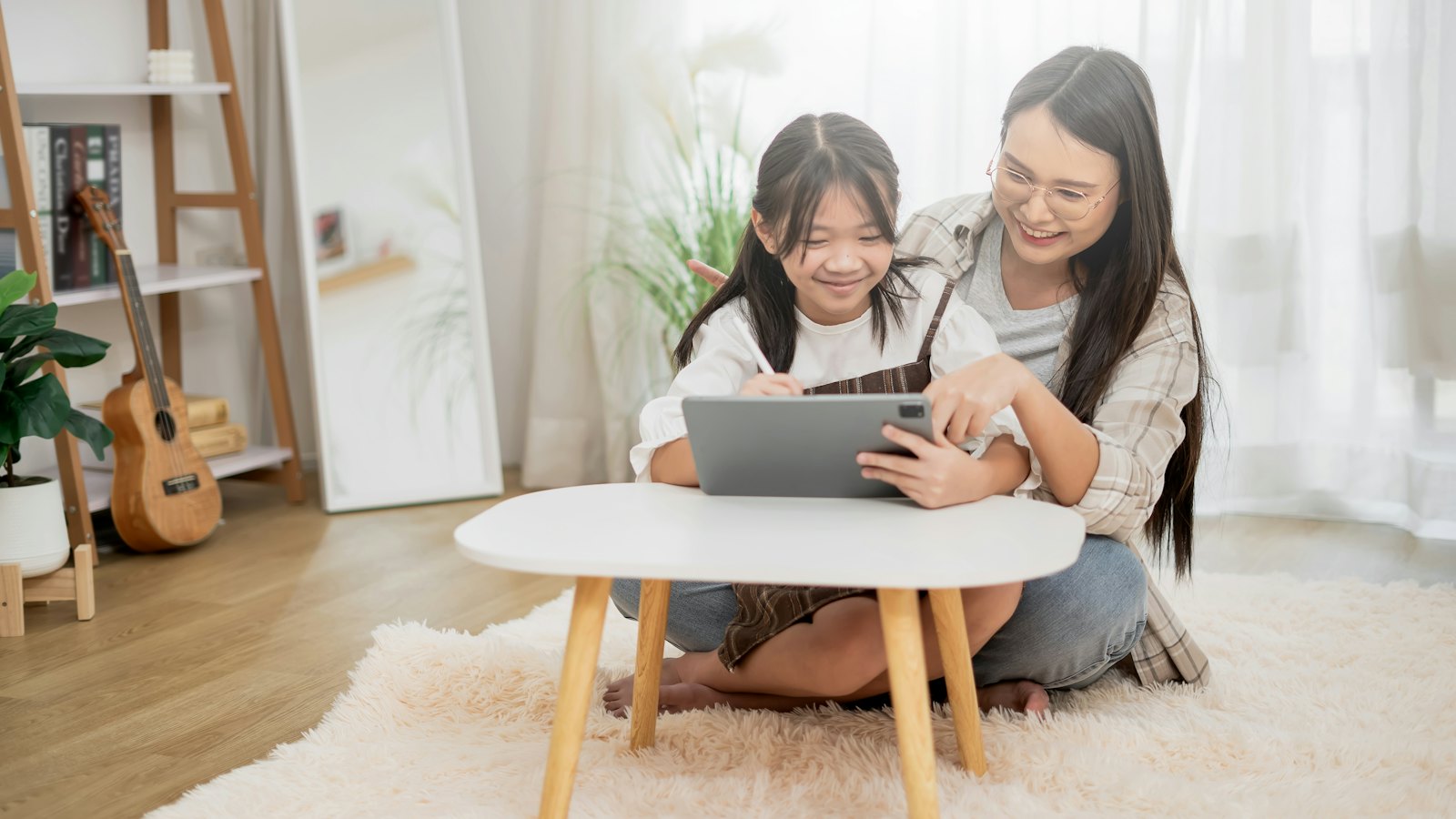 A mother and daughter sitting on the floor looking at a tablet together