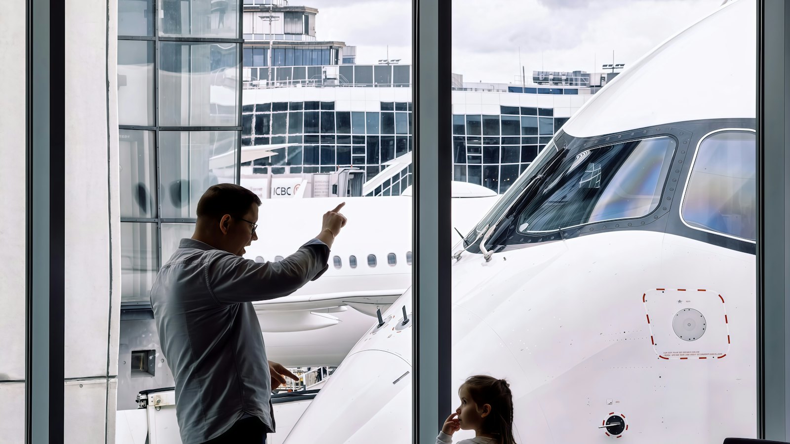 A father pointing at an aeroplane through an airport window