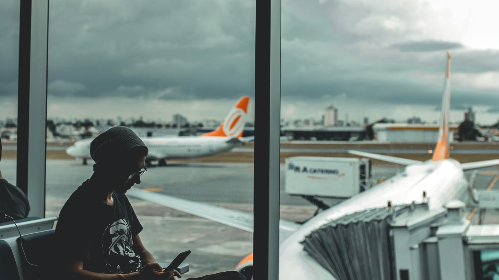 A traveller using a phone by an airport window with planes outside