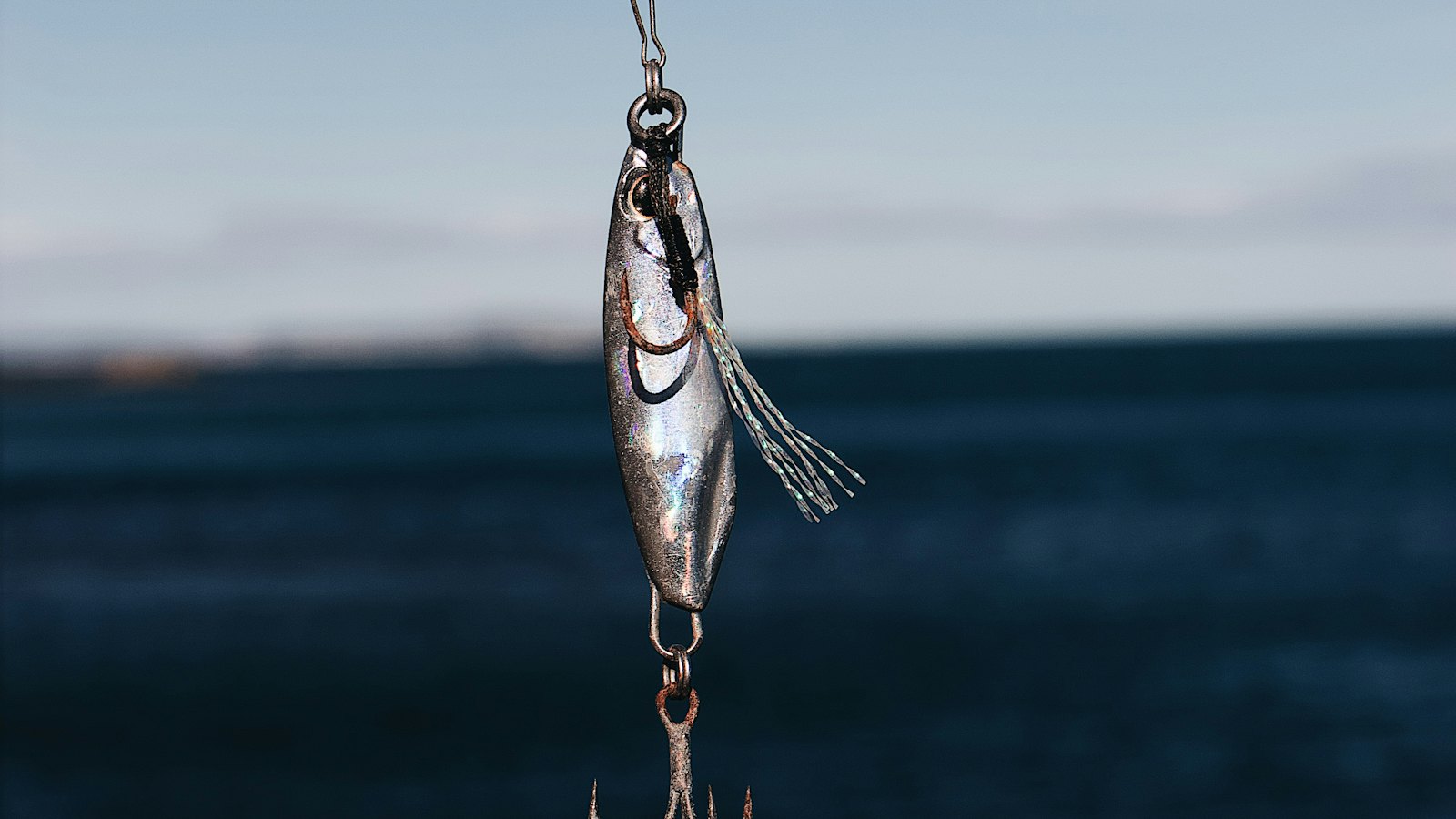 A silver fishing lure hanging over the sea