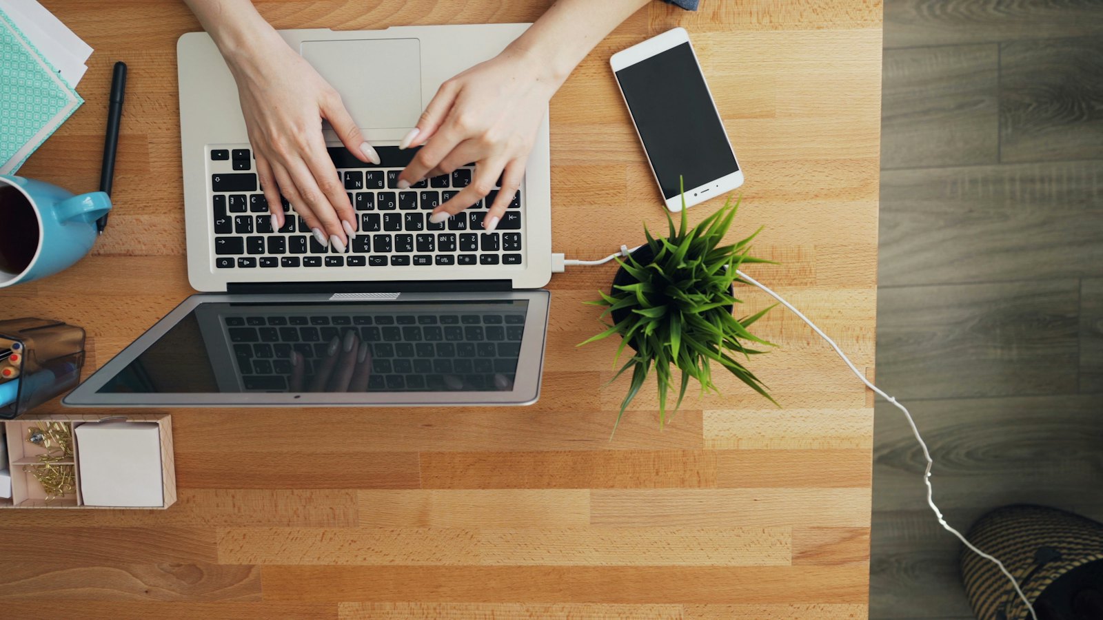 An overhead view of hands typing on a laptop at a wooden desk