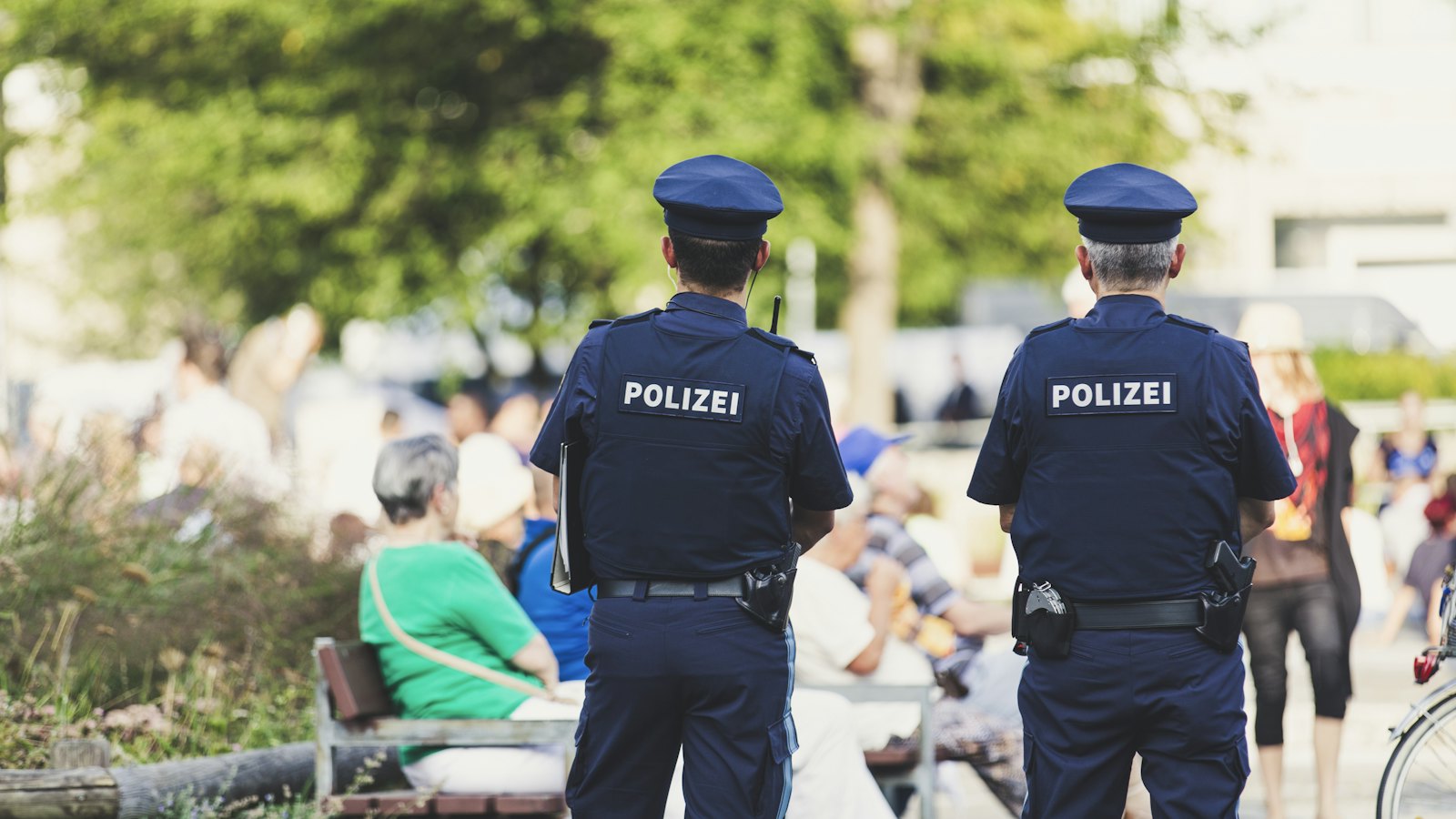 Two police officers seen from behind as they walk through a busy park