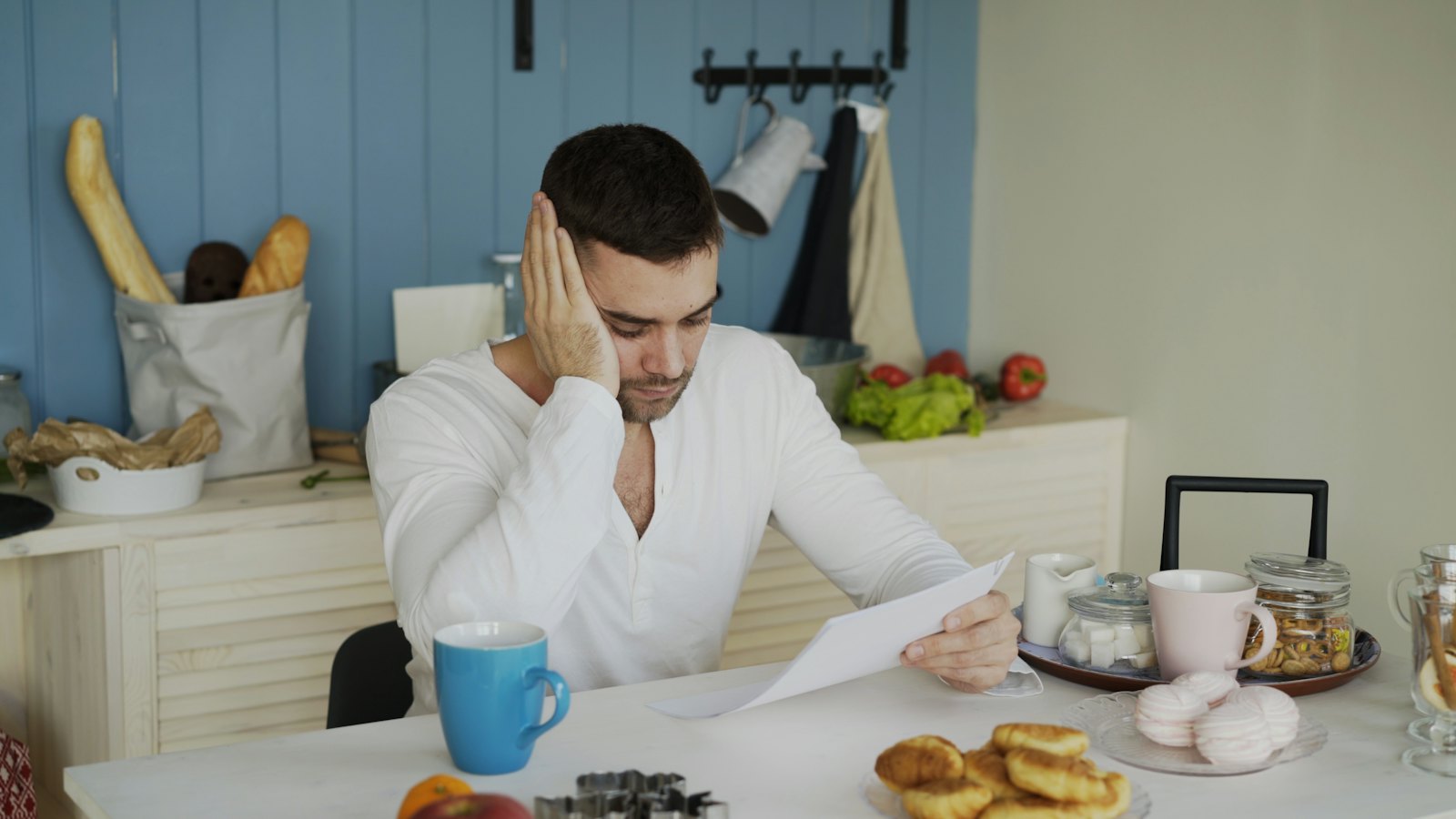 A worried man reading a letter at his kitchen table