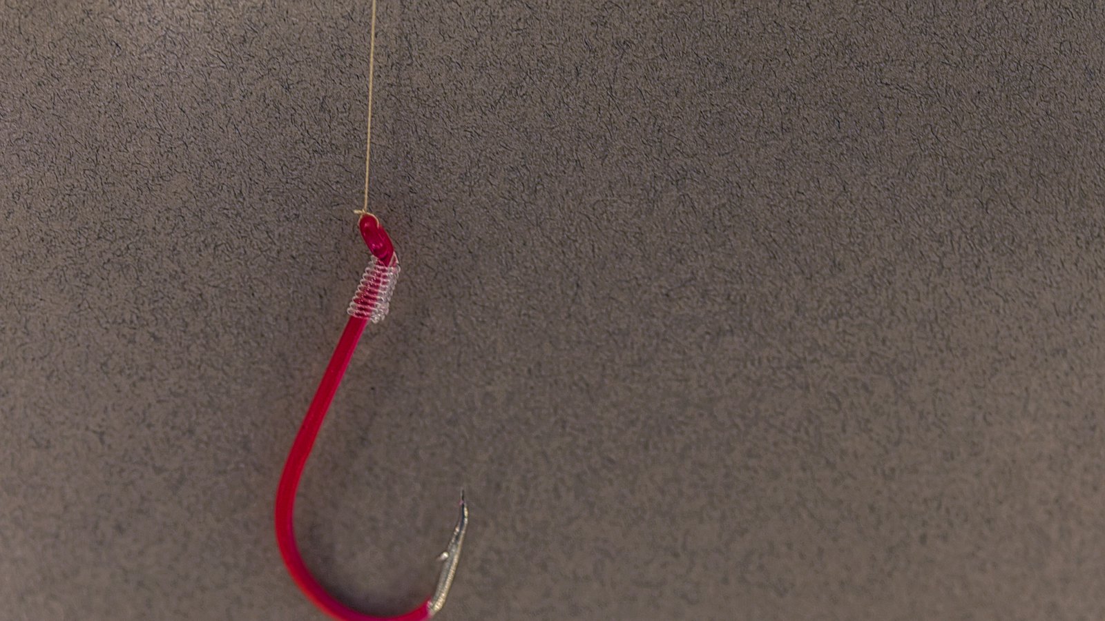 A red fishing hook hanging against a grey background