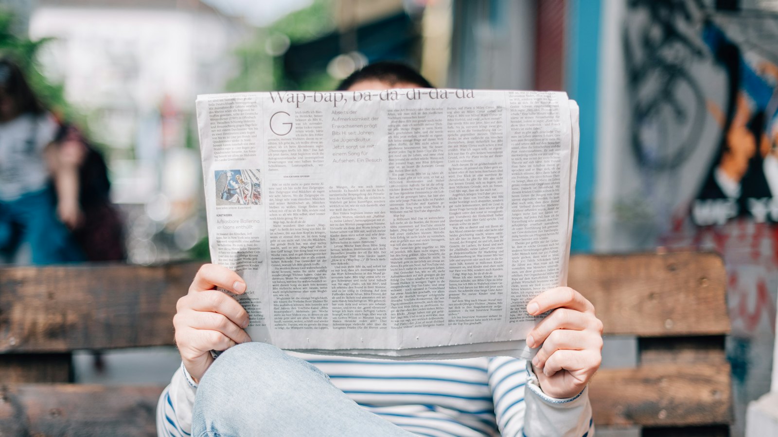 A person reading a newspaper on a bench