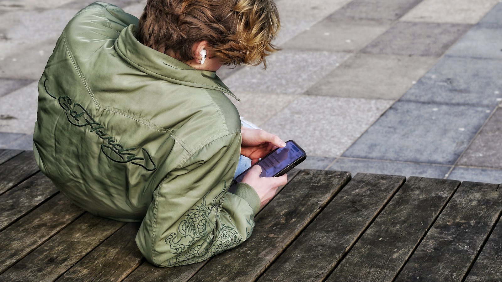 A teenager looking at a phone on a bench