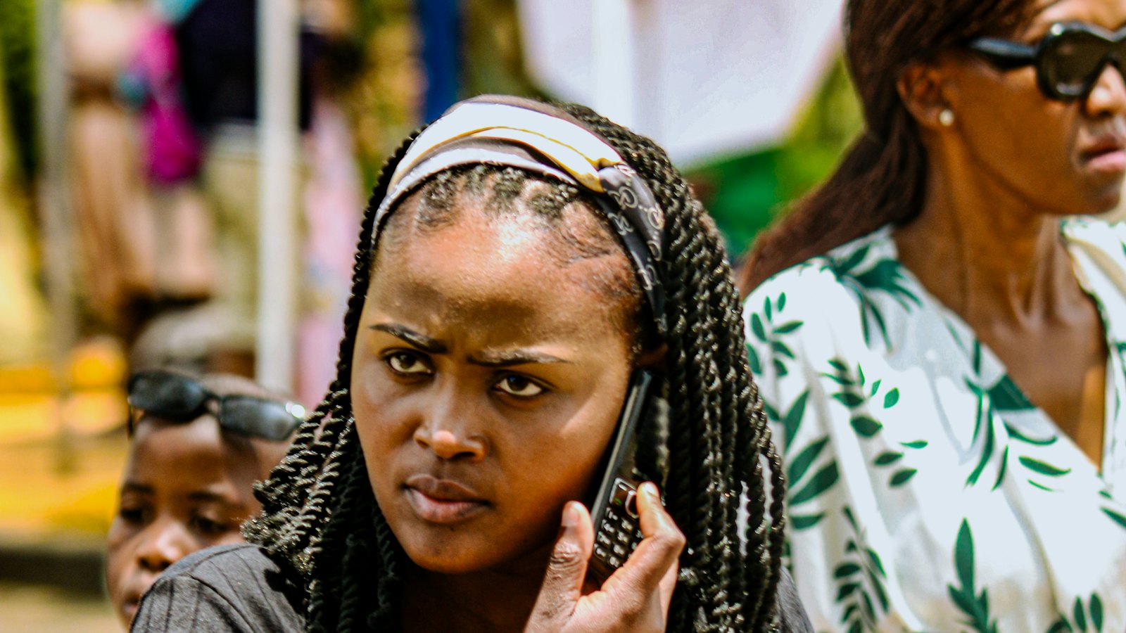 A woman in a busy market listening on her phone with a doubtful expression